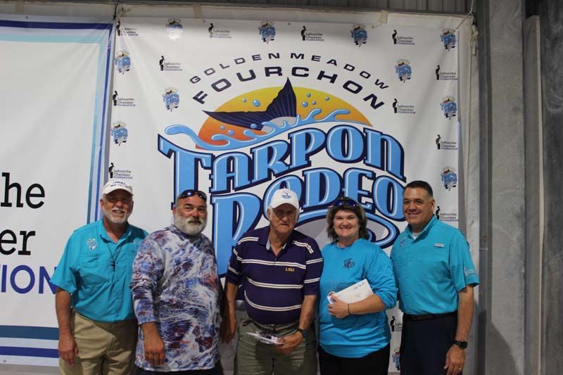 A group of people standing in front of a tarpon rodeo banner
