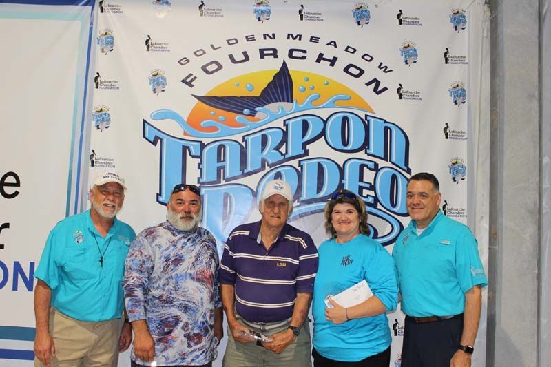 A group of people standing in front of a tarpon rodeo banner
