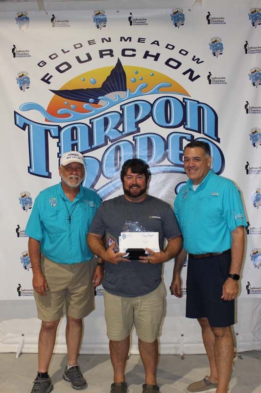 Three men standing in front of a tarpon rodeo banner