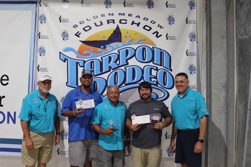 A group of men are standing in front of a tarpon rodeo banner.