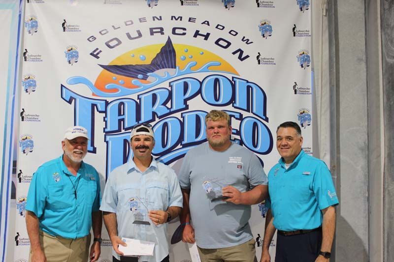 Four men standing in front of a tarpon rodeo banner