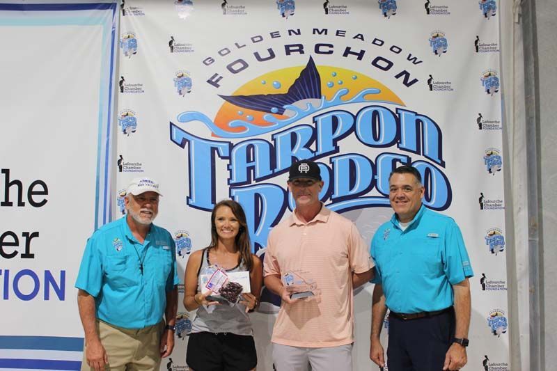 A group of people standing in front of a tarpon rodeo banner