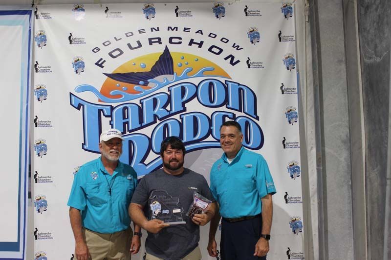 Three men are standing in front of a tarpon rodeo banner