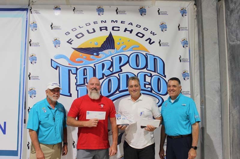 A group of men standing in front of a tarpon rodeo banner