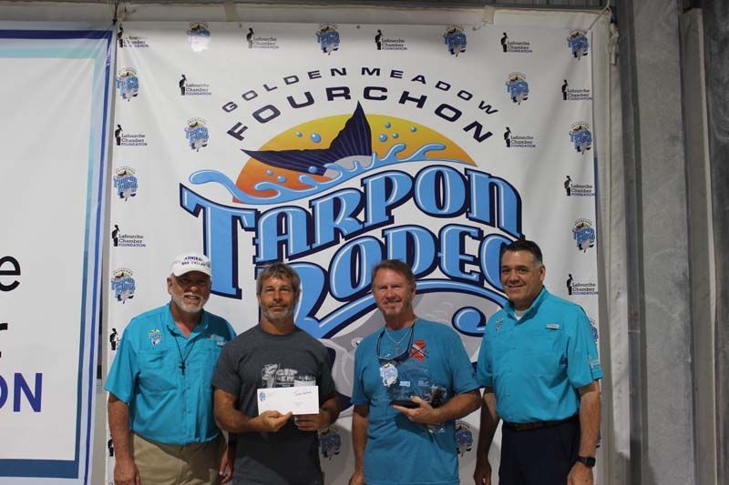 Four men standing in front of a tarpon rodeo banner