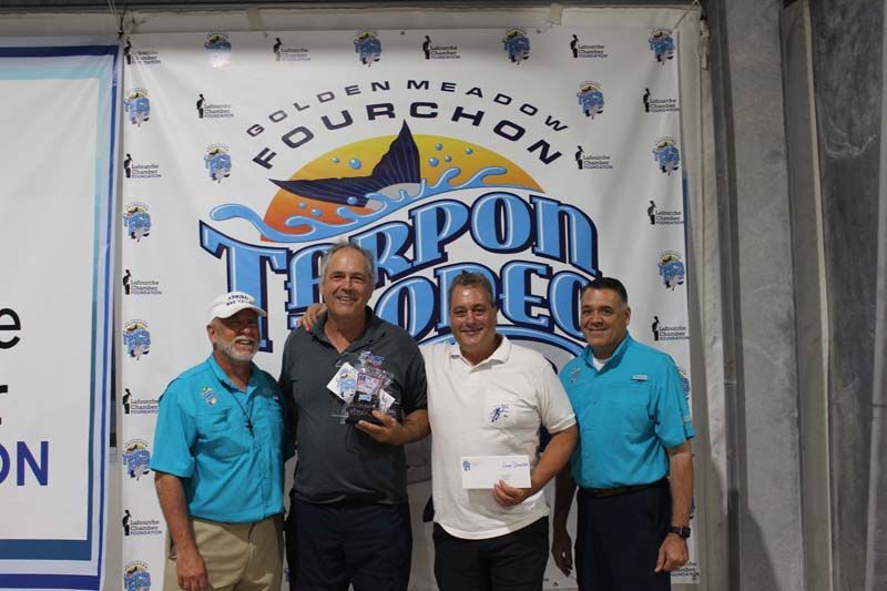Four men are posing for a picture in front of a banner that says fourchon