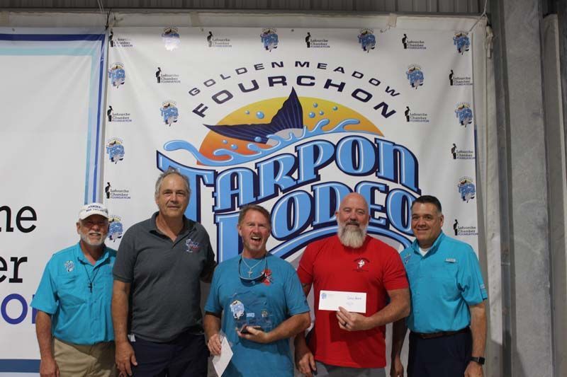 A group of men standing in front of a tarpon rodeo banner