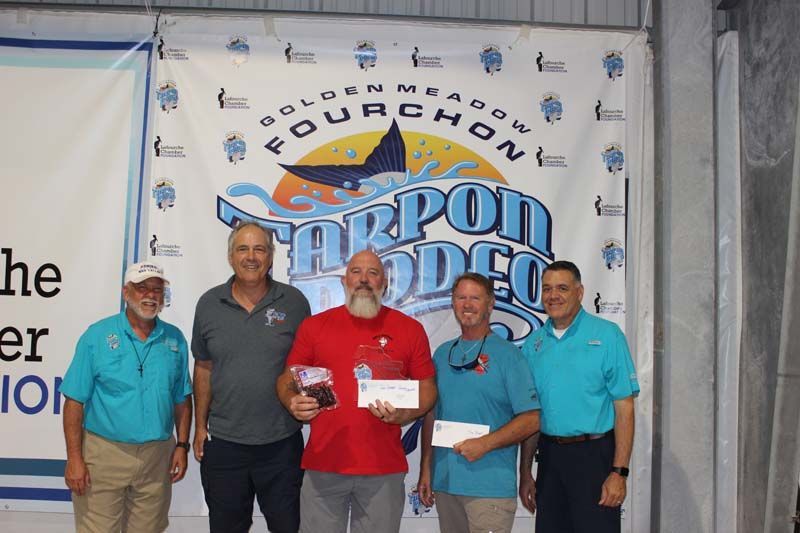 A group of men standing in front of a banner that says fourchon tarpon rodeo