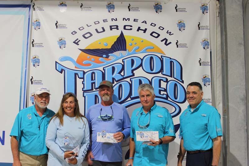 A group of people standing in front of a tarpon rodeo banner.