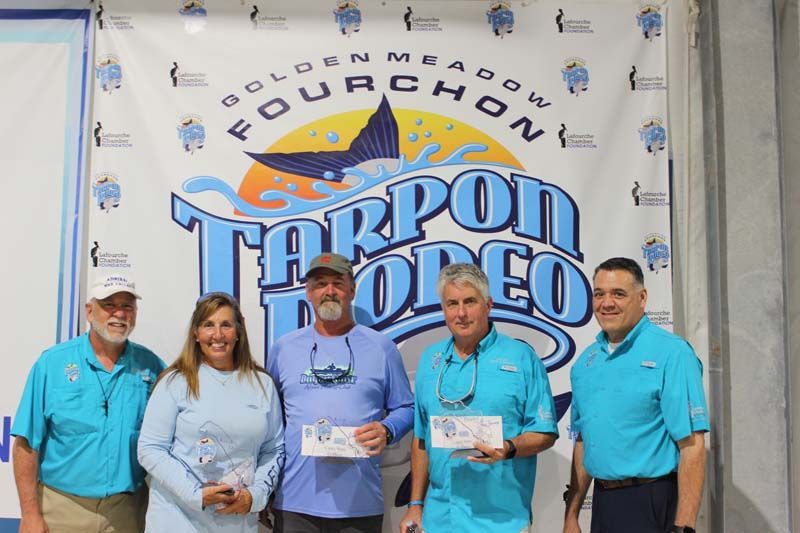 A group of people standing in front of a tarpon rodeo banner.