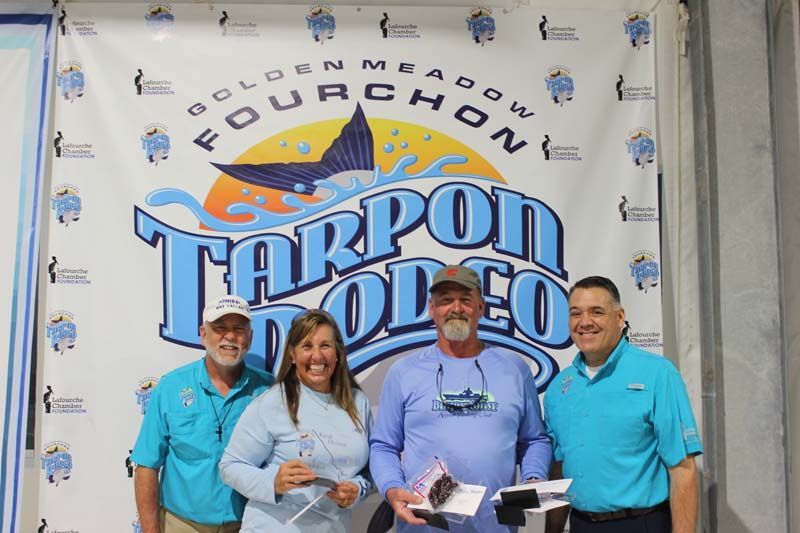 A group of people standing in front of a tarpon rodeo banner