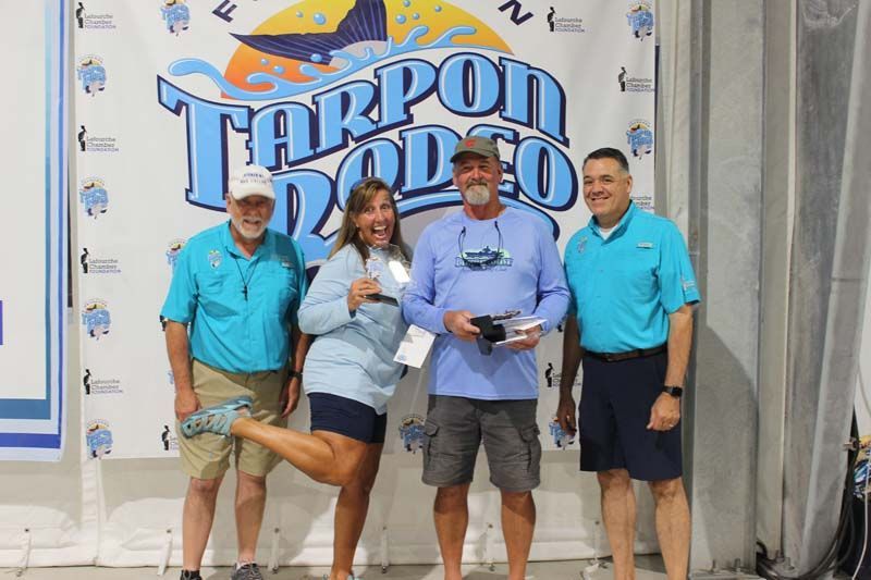 A group of people standing in front of a tarpon rodeo banner.