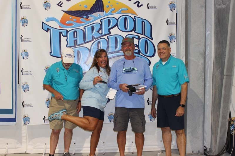 A group of people standing in front of a tarpon rodeo banner