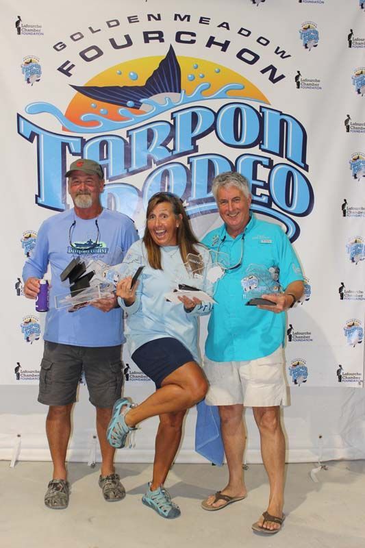 Three people standing in front of a banner that says tarpon rodeo