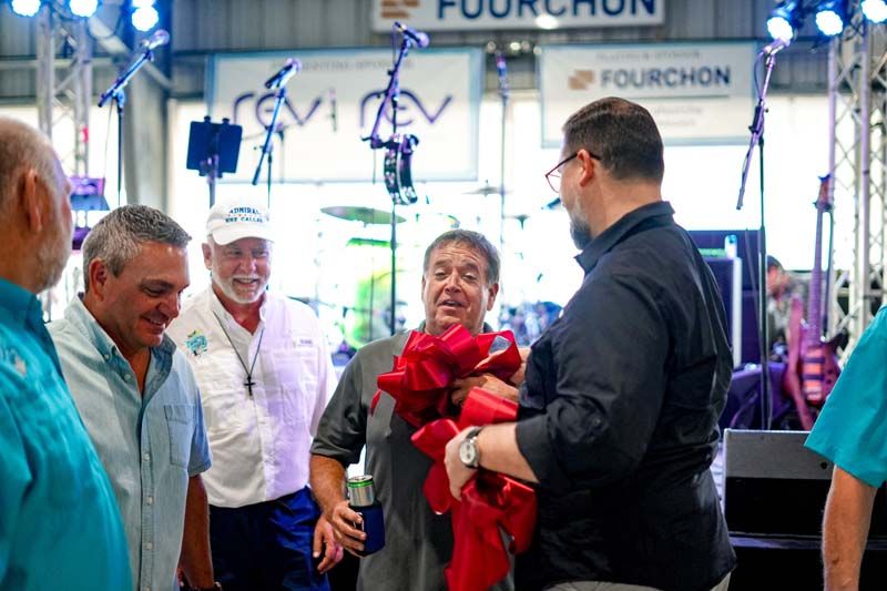 A group of men are standing around a man holding a red bow.