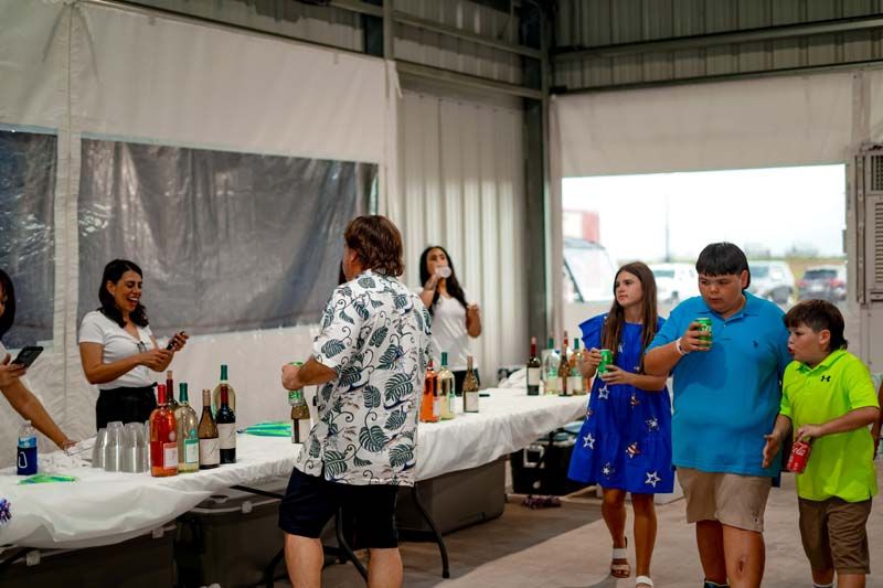 A group of people are standing around a table with bottles of wine.