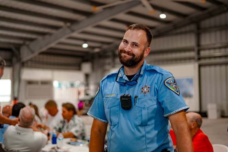 A police officer is smiling while standing in front of a group of people.