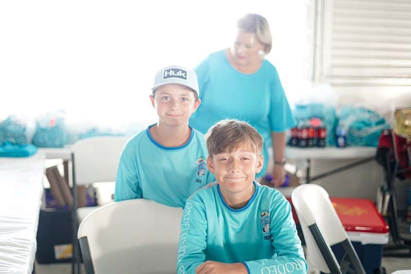 A woman is standing behind two boys sitting in chairs.