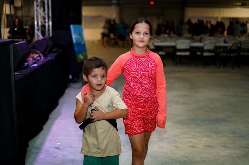 A boy and a girl are walking down a runway at a fashion show.