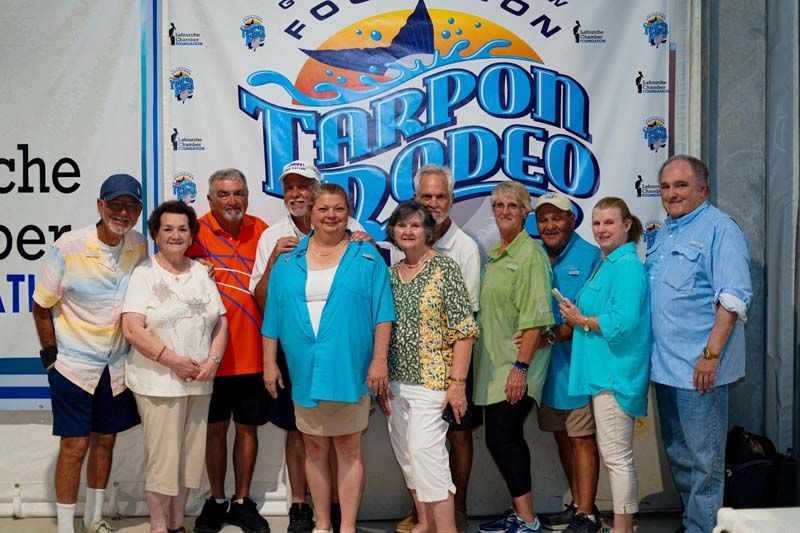 A group of people standing in front of a tarpon rodeo banner