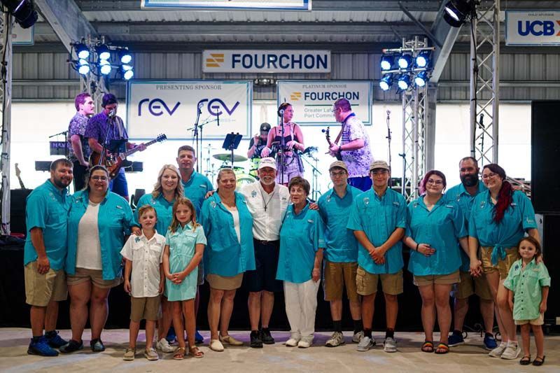 A large group of people are posing for a picture in front of a band on stage.