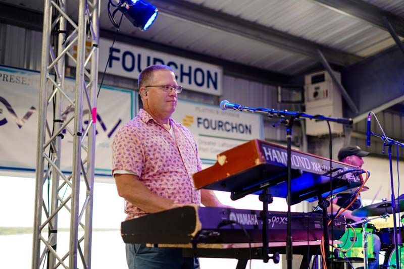 A man is playing a keyboard on a stage in front of a microphone.