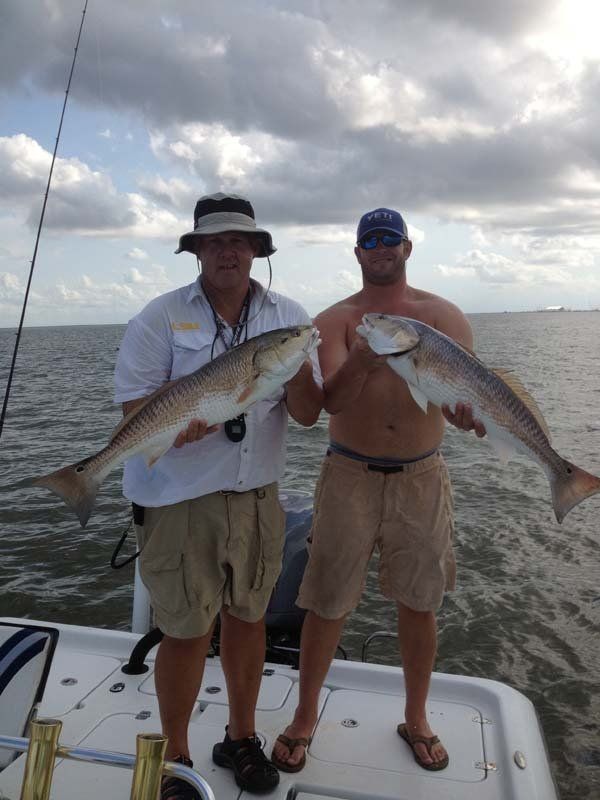 Two men are standing on a boat holding two large fish.