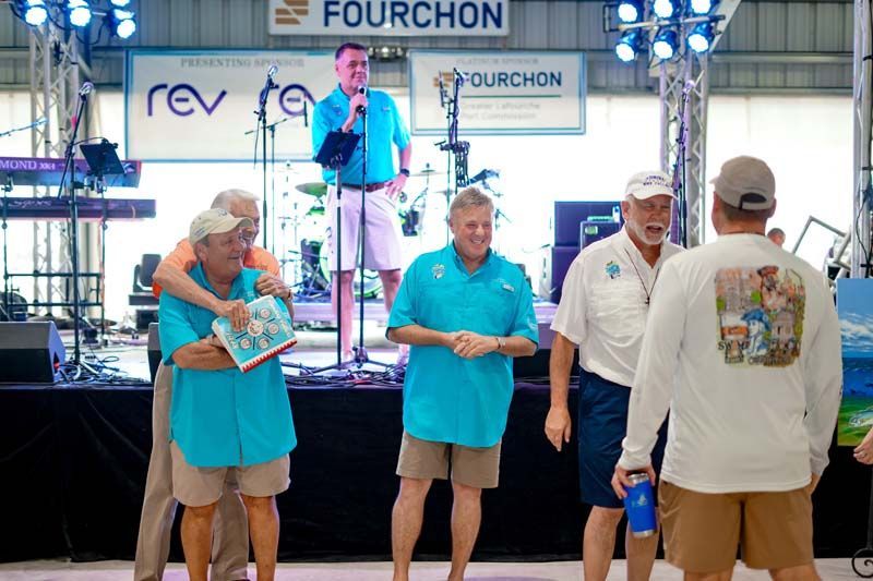 A group of men are standing on a stage in front of a sign that says fourchon