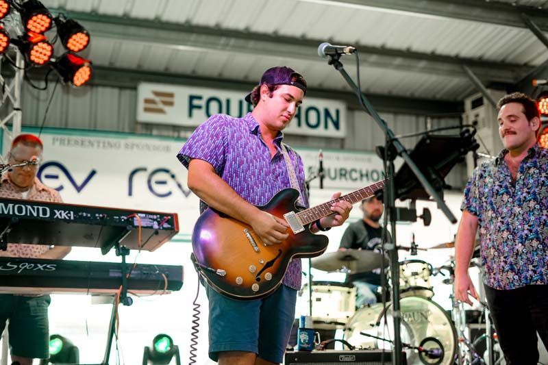 A man is playing a guitar on stage with a band behind him.