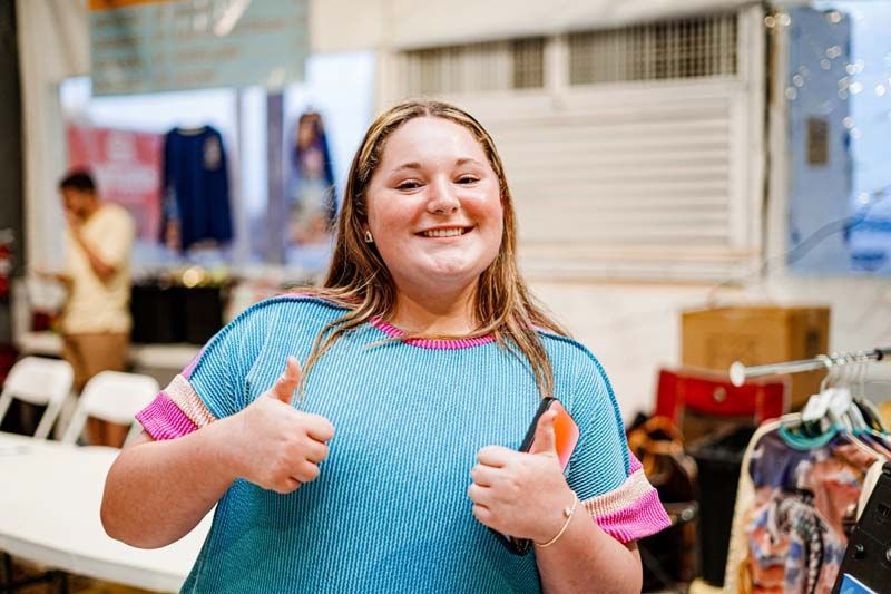 A young girl in a blue shirt is giving two thumbs up.