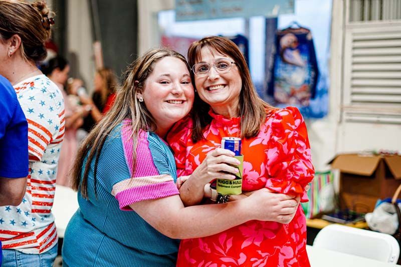 Two women are hugging each other while holding a can of soda.