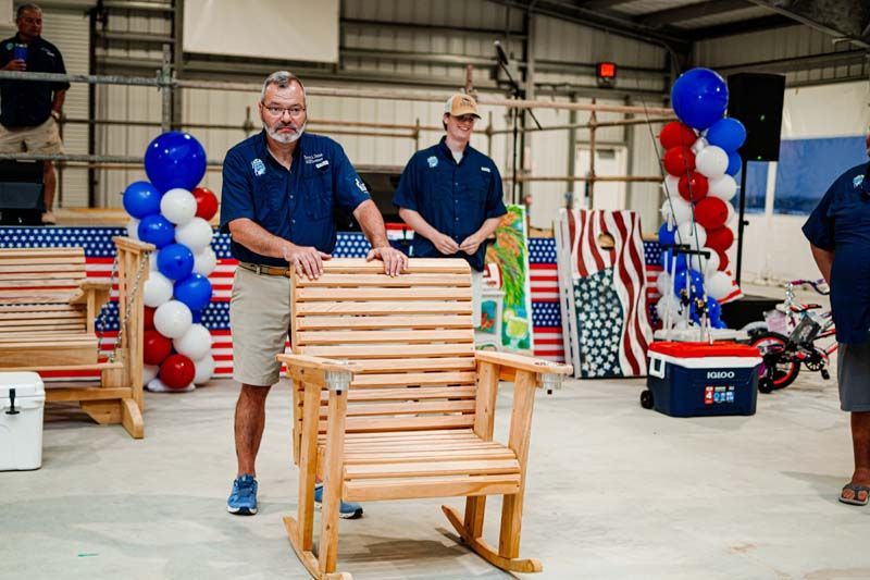 Two men are standing next to a wooden rocking chair.