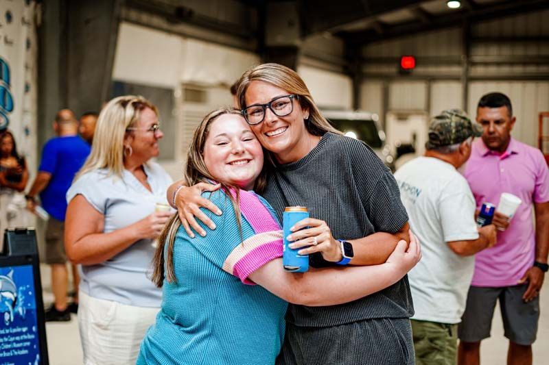 Two women are hugging each other while holding a can of beer.