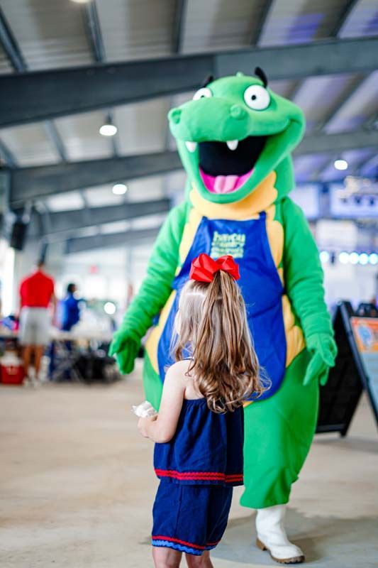 A little girl is standing next to a green alligator mascot.