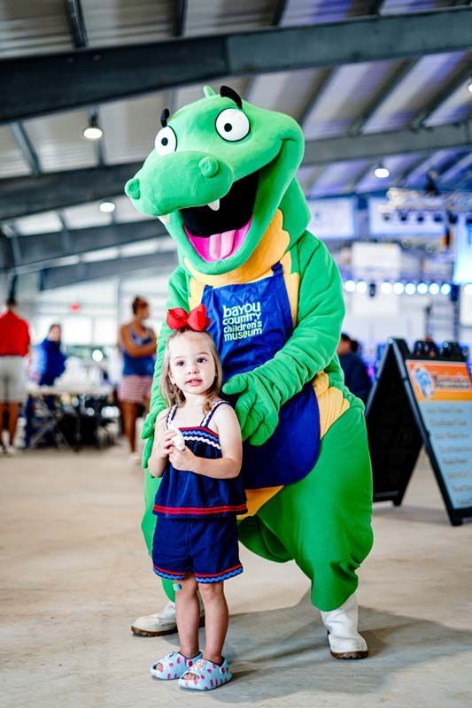 A little girl is standing next to a green dinosaur mascot.