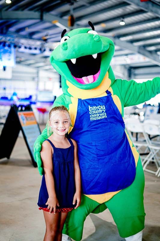 A little girl is posing for a picture with a green mascot.