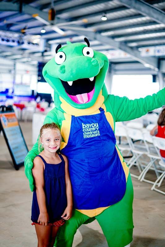 A little girl is posing for a picture with a green alligator mascot.
