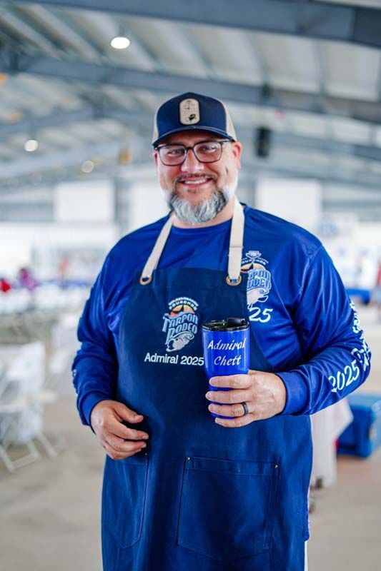 A man in a blue shirt and apron is holding a cup.