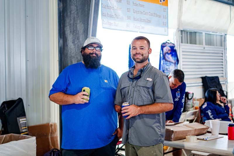 Two men are standing next to each other in a room holding drinks.