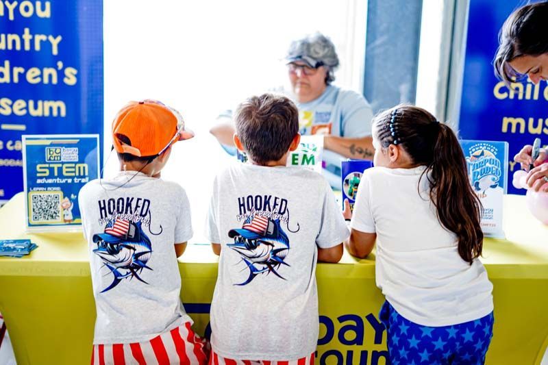 A group of children are sitting at a table wearing hooked shirts