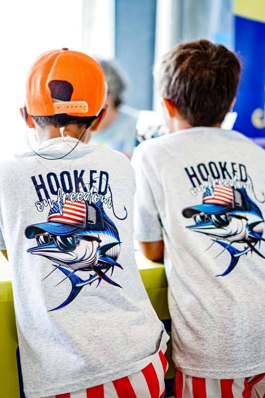 Two young boys wearing hooked t-shirts are sitting on a couch.