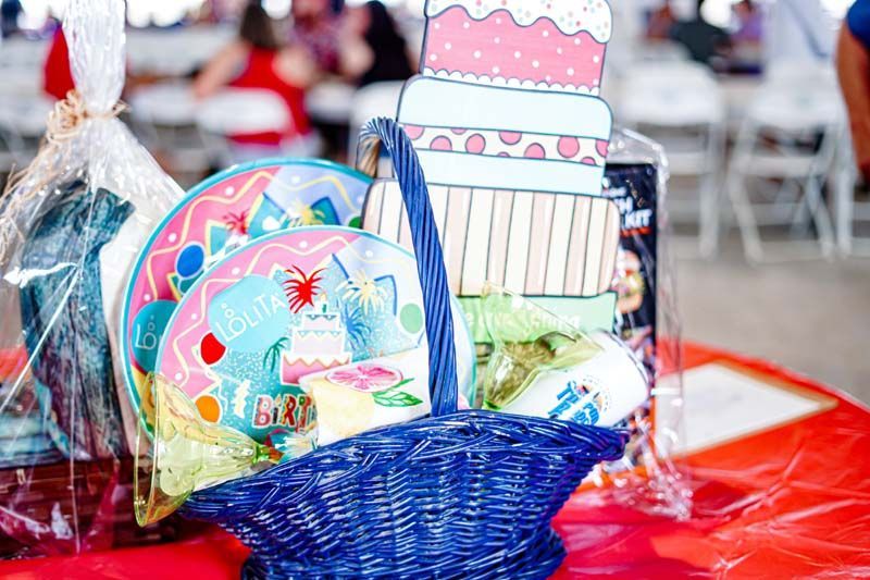 A basket filled with birthday plates and a cake on a table.