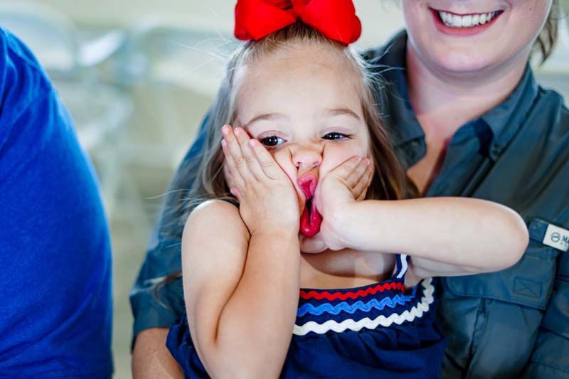 A little girl with a red bow on her head is being held by a woman.