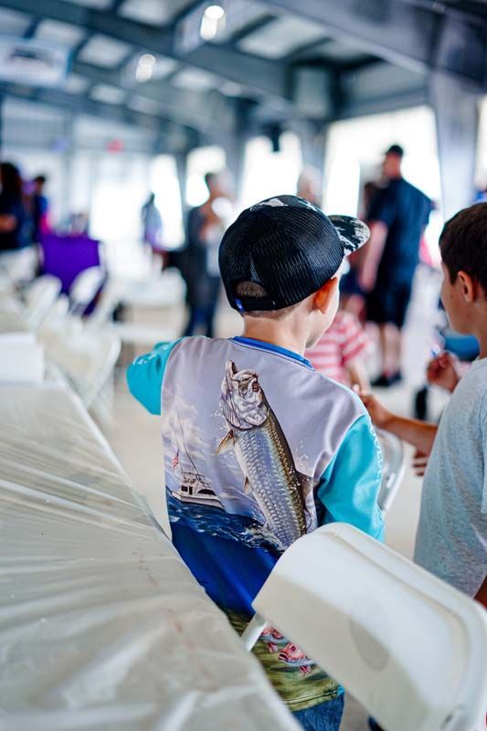 A boy wearing a shirt with a fish on it is sitting in a chair.