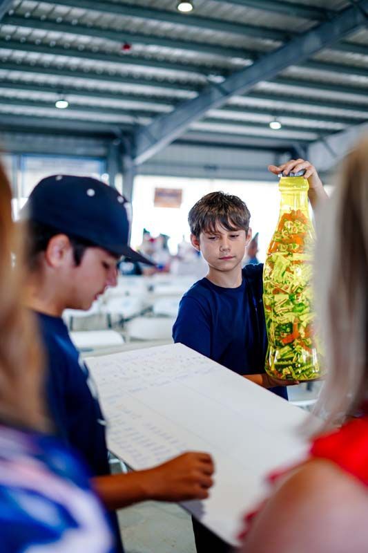 A boy is holding a large bottle of vegetables.