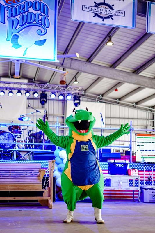 A mascot in a green and yellow dinosaur costume is standing in a building.