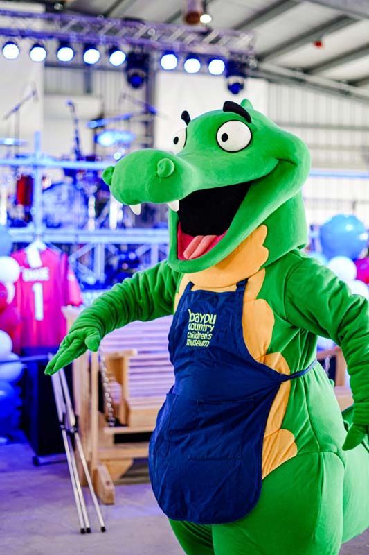 A green dinosaur mascot is standing in a warehouse holding a pair of skis.