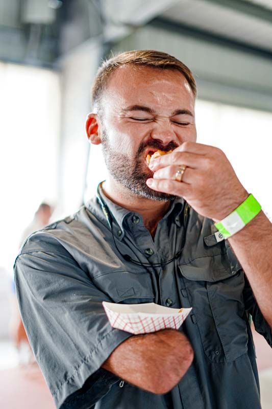 A man with a beard is eating a hot dog with his eyes closed.