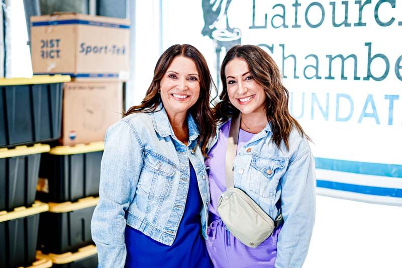 Two women are posing for a picture in front of a sign that says latourc chamber foundation.