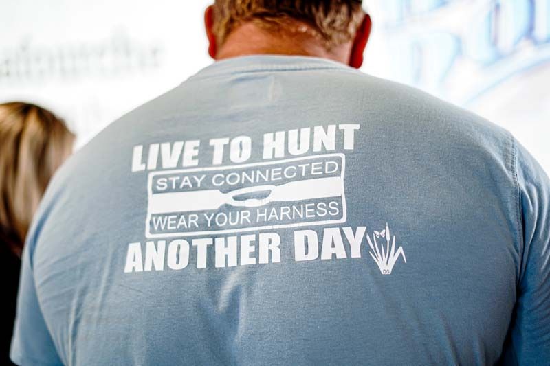 A man wearing a t-shirt that says live to hunt stay connected wear your harness another day